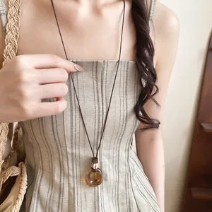 Detailed close-up of amber resin oval pendant necklace featuring a dark brown leather cord