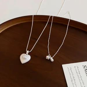 Close-up of elegant silver peanut and heart pearl necklaces on a dark wood tray.