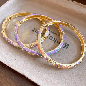 Close-up detail of three gold-plated enamel flower bangles with elegant rhinestone accents