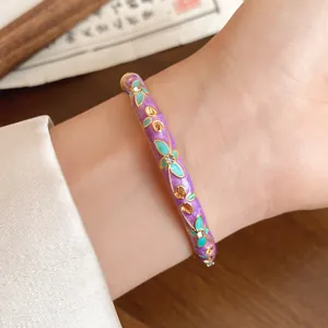 Detailed view of a purple enamel bangle featuring teal flowers and small crystals on a wrist