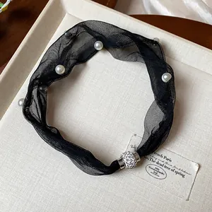 Dettaglio collana in rete nera con perle e una chiusura magnetica con strass brillanti