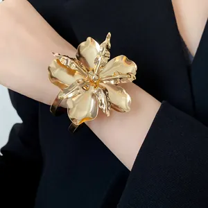 Close-up of a bold gold flower cuff bracelet worn on a black blazer sleeve for a luxury look