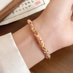 Close-up of a vintage gold floral bangle with purple enamel and small rhinestones on a wrist.