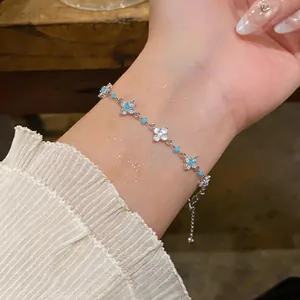 Nahaufnahme eines silbernen Zirkonia-Armbands mit Kleeblatt-Anhängern und blauen Perlen am Handgelenk