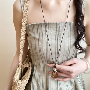 Detailed view of a resin donut pendant on a leather cord worn with a summer outfit.