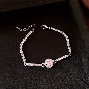 Dettaglio di un bracciale argentato con zircone rosa centrale in scatola nera.
