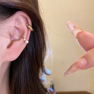 Detailed view of elegant gold-toned ear cuffs with pearl and zircon on model's ear