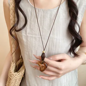 Detailed view of a minimalist amber resin oval pendant on a brown leather cord necklace.