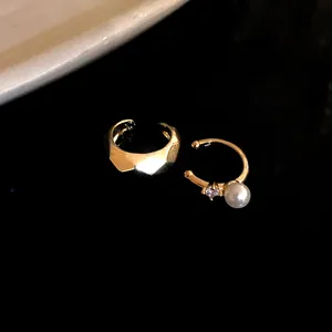 Close-up of gold geometric ear cuff and pearl zircon cuff on black background.