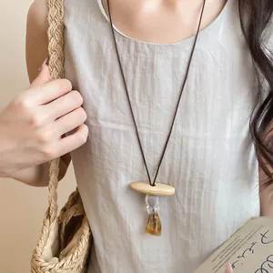Close-up of a minimalist resin pendant necklace with leather cord worn on a linen top