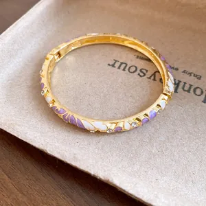 Close-up of vintage gold bangle with purple enamel flower patterns and rhinestones.