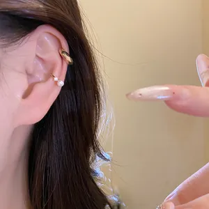 Close-up detail of minimalist gold ear cuffs featuring pearl and zircon on model's ear