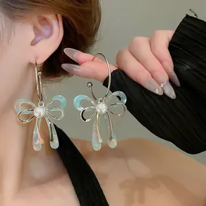 Close-up of elegant silver needle bow earrings with light blue patterns and a central pearl
