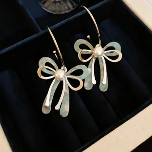 Detail view of bow earrings with green marble acrylic and white pearl in a velvet box