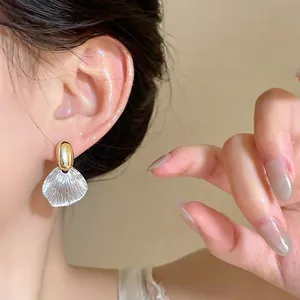 Close-up of elegant gold stud earring with a textured clear leaf-shaped drop on ear