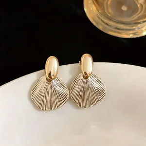 Detailed macro view of elegant golden French style textured leaf earrings on a white plate