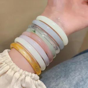 Détail de joncs colorés translucides empilés au poignet, montrant des textures élégantes.
