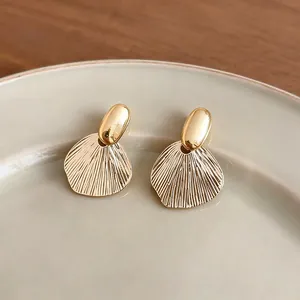 Elegant French style gold leaf textured stud earrings on a minimalist ceramic plate