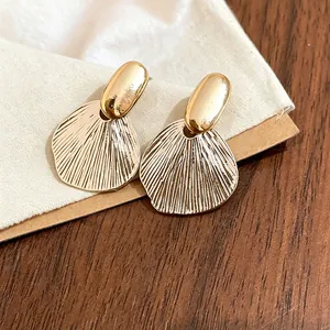 Close-up of French-style gold textured leaf stud earrings on a fabric background.