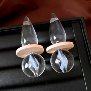 Close-up of minimalist transparent teardrop earrings with wooden disc and glass sphere