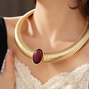 Dettaglio di un girocollo dorato a coste con una pietra ovale in resina rosso scuro.