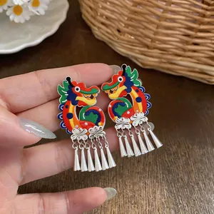 Detailed view of handmade knitted dragon earrings with silver tassels held in hand