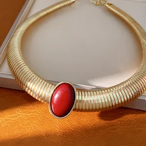 Dettaglio di una collana girocollo dorata a coste con grande pietra in resina rossa.