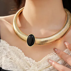 Dettaglio di un girocollo dorato vintage con una grande pietra in resina nera su una modella.