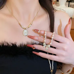 Close-up of zircon bow and pearl necklace with a crystal-encrusted letter H pendant.