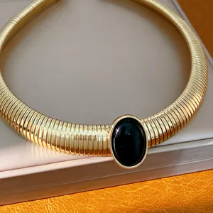 Dettaglio di un girocollo dorato a coste con una grande pietra ovale in resina nera.