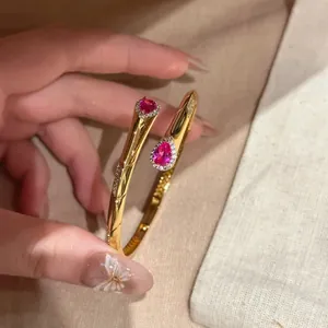 Dettaglio del bracciale rigido dorato con zirconi rosa a forma di pera e un halo