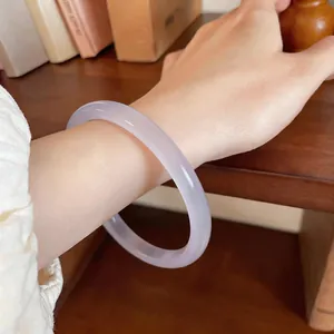 Gros plan d'un bracelet jonc en calcédoine blanche translucide au poignet d'une femme élégante