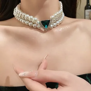 Close-up of vintage triple-layer pearl choker with a sparkling green triangle gemstone