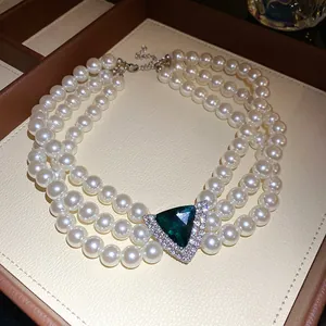 Detail view of a vintage three-layer pearl choker with a sparkling green triangle gem.