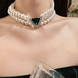 Detailed view of a three-row pearl choker with a green triangular gemstone.
