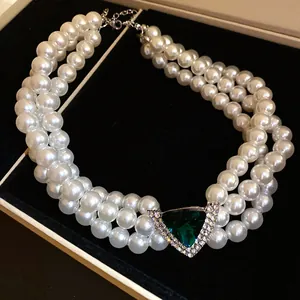 Detailed macro view of triple-layer pearl choker featuring a green triangle gemstone pendant