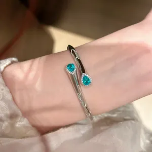 Dettaglio di un bracciale a fascia in argento con pietre di zircone verde a goccia.