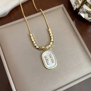 Detailed macro view of elegant gold necklace featuring rhinestone letter H pearl pendant