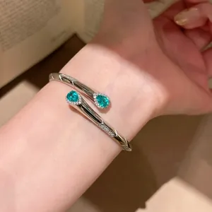 Dettaglio di un elegante bracciale rigido argento con scintillanti zirconi verdi a goccia.