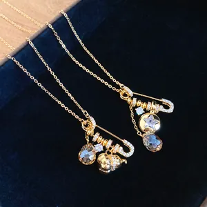 Detailed macro view of 24k gold plated safety pin pendant with zircon and gourd charms