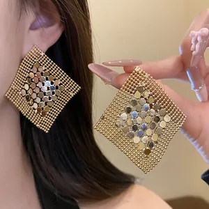 Macro detail of oversized gold geometric mesh sequin earrings worn on ear and held by hand