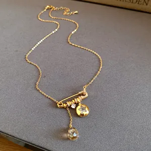 Close-up of 24k gold plated necklace with safety pin pendant and water drop crystal