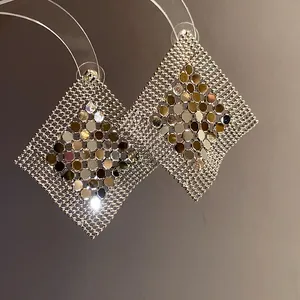 Close-up of geometric sequin mesh earrings with shimmering metallic finish and fringe design.