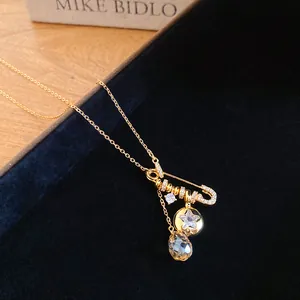 Detail view of 24k gold-plated safety pin necklace with zircon star and teardrop charms