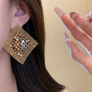Detailed macro view of oversized gold geometric mesh earrings with sequin fringe design