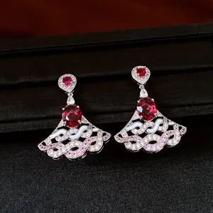 Close-up of fan-shaped drop earrings featuring red oval zircon and silver filigree