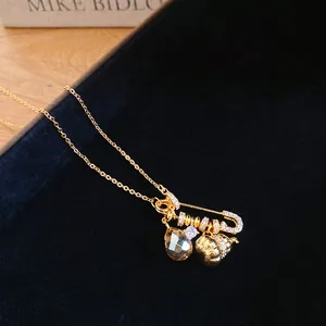 Detail view of 24k gold plated safety pin necklace with zircon gourd and drop charms
