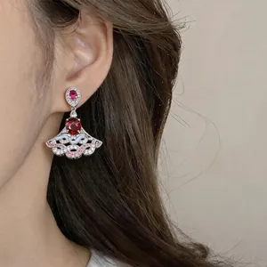 Close-up detail of an elegant fan-shaped drop earring with red oval zircon on model's ear