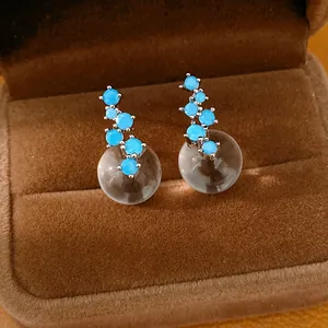 Detailed view of blue zircon earrings with clear resin spheres in brown velvet box.