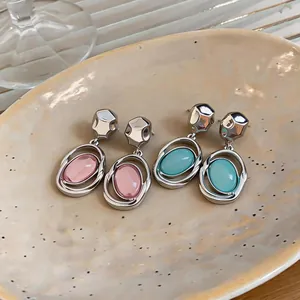 Close-up of silver-tone earrings with pink and blue oval stones on a ceramic plate